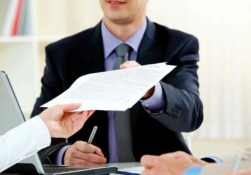 A professionally dressed man hands documents across a table