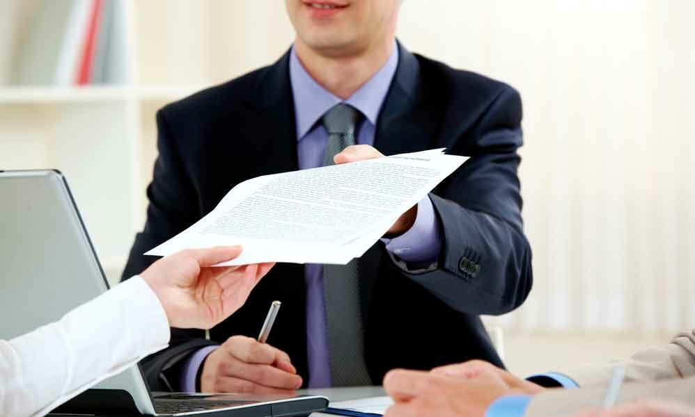 A professionally dressed man hands documents across a table